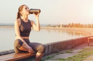 Woman sitting by the lake drinking from an ice shaker bottle